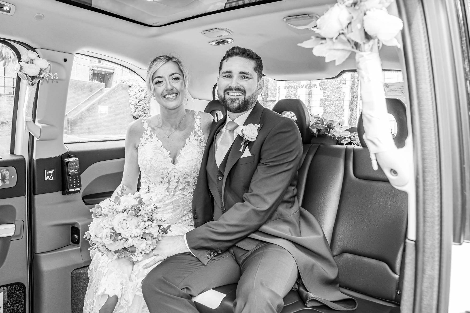 Bride and groom sit in wedding car.