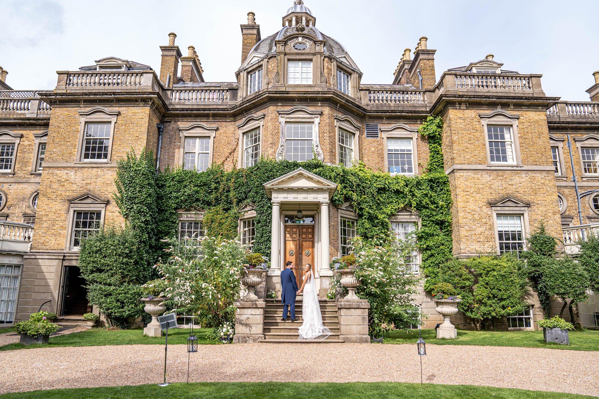 Bride and groom stand on the steps of Hampton Court House.