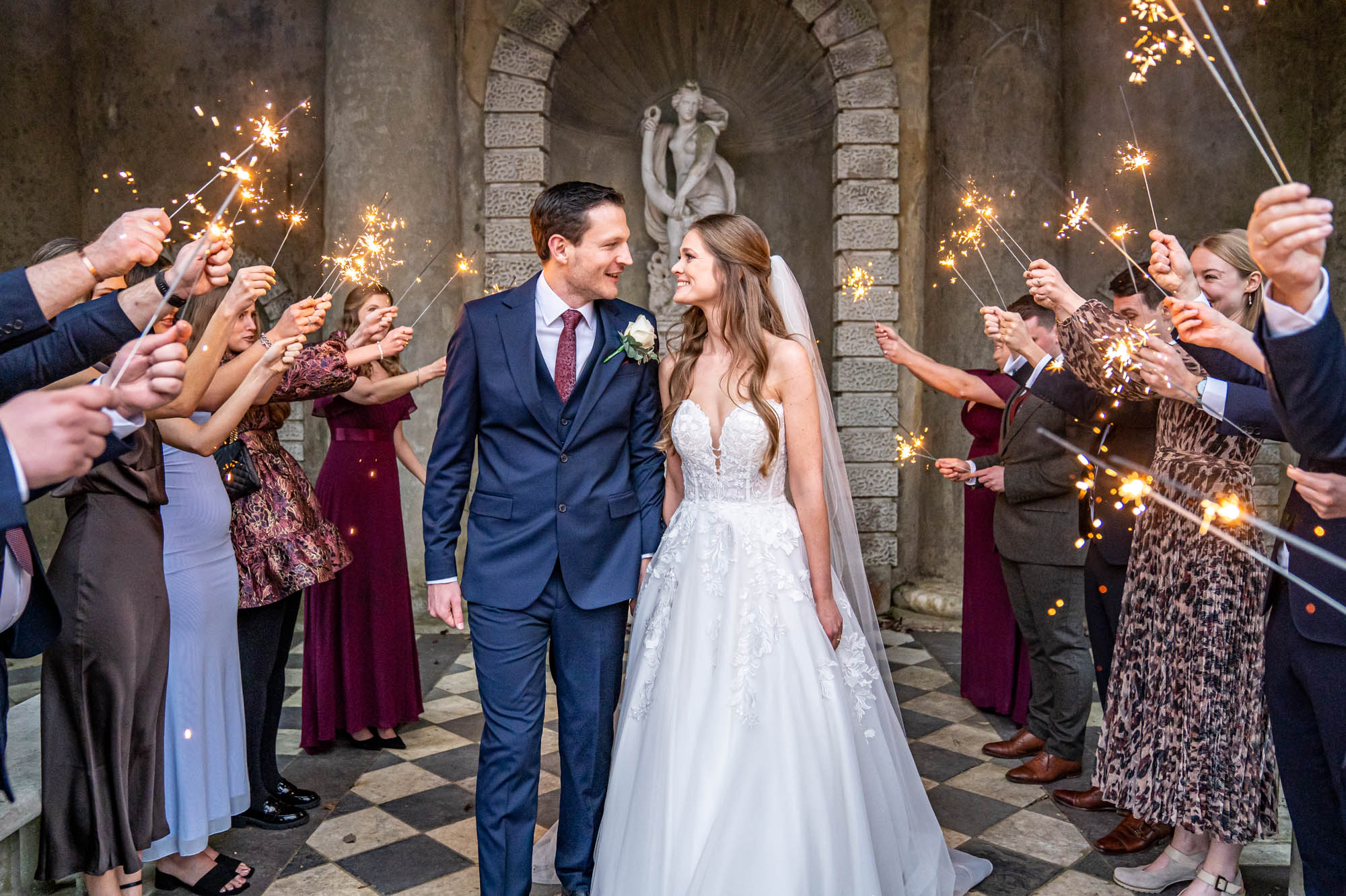 Wedding guests wave sparklers as newlyweds walk together.