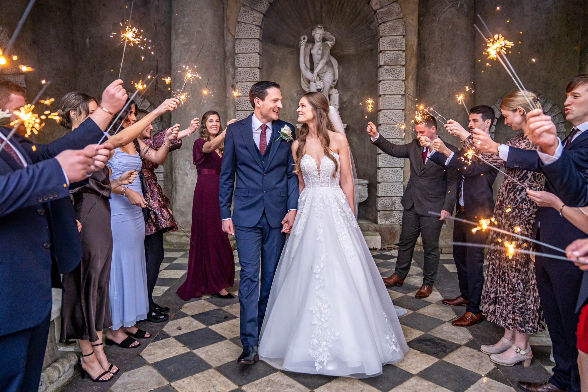 Groom walks with his bride through the sparklers exit under the Italian temple at Wotton House.